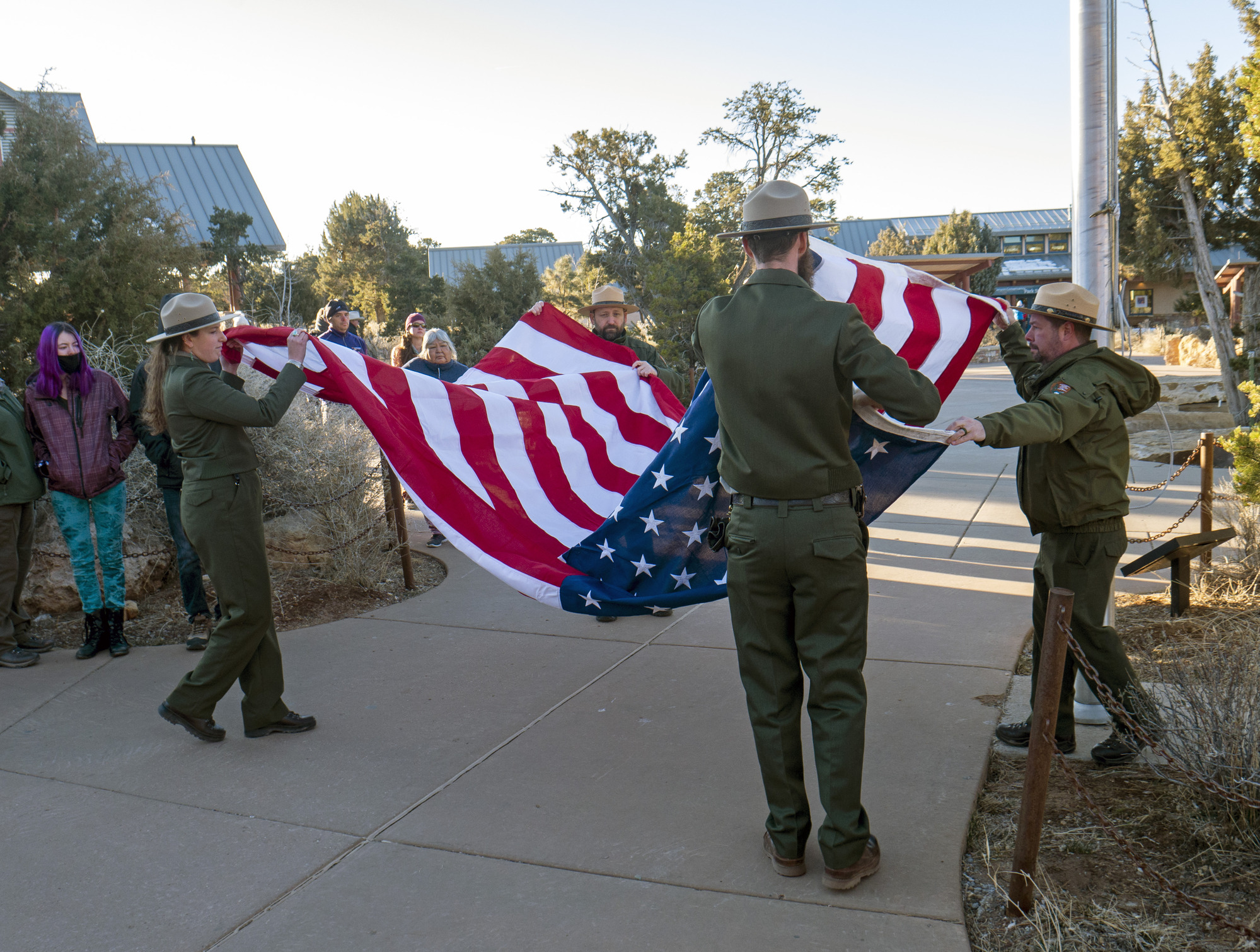 During an outdoor memorial ceremony. four park rangers are taking down an large American flag, and beginning to fold it.