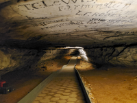 Historic signatures decorate the ceiling of the cave with a paved trail leading beneath them. 