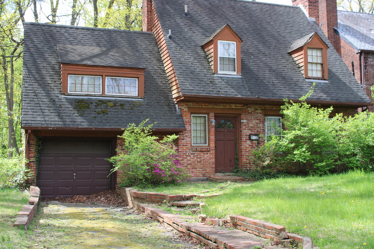 a two-story brick house with a garage, a long-slanted shingle roof, and dormers. 