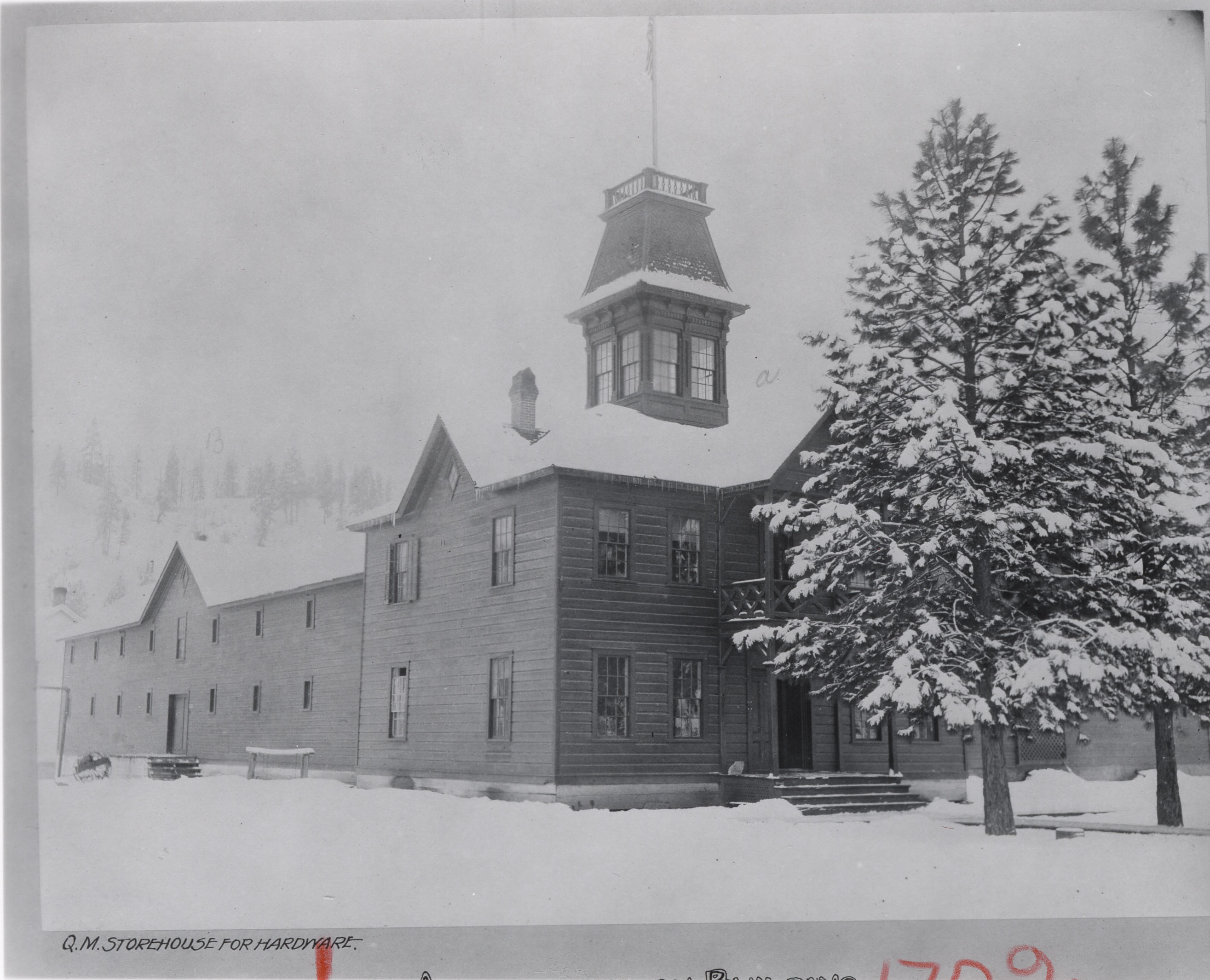 Black and white photograph of a multi-story wooden building with tower in the snow
