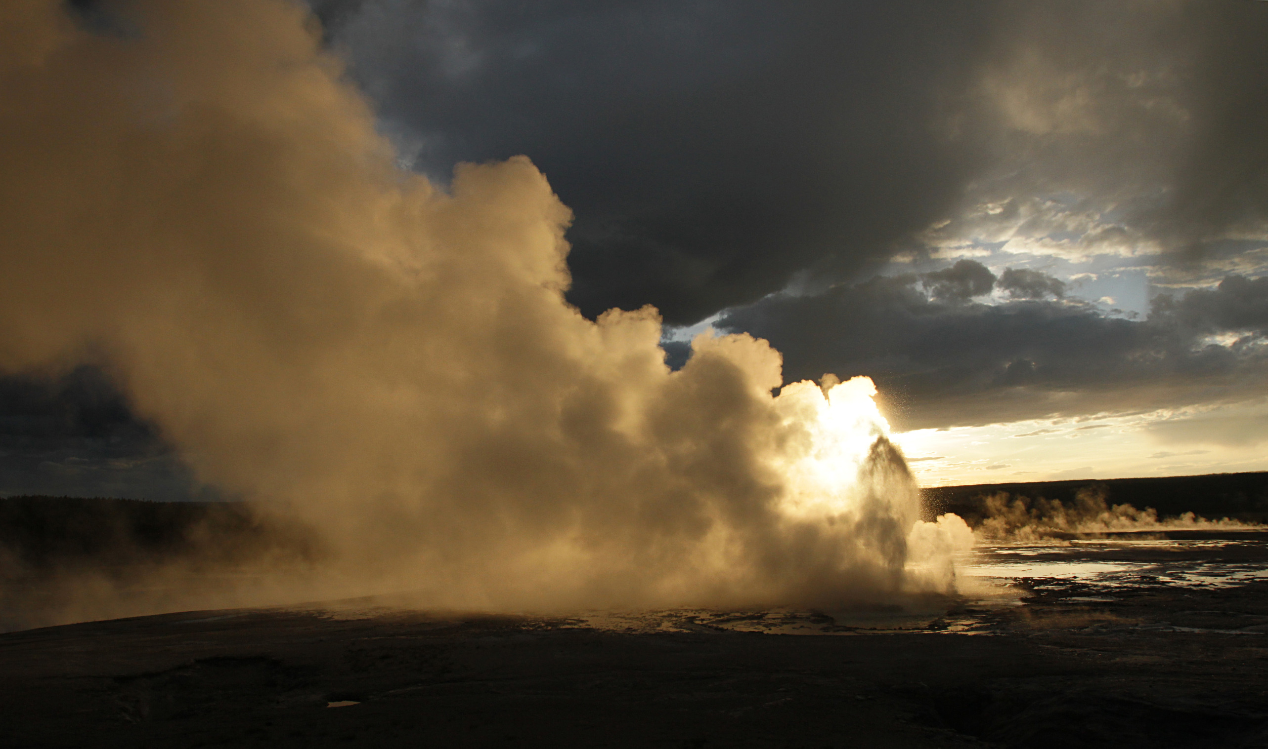 The sun shines behind a geyser eruption