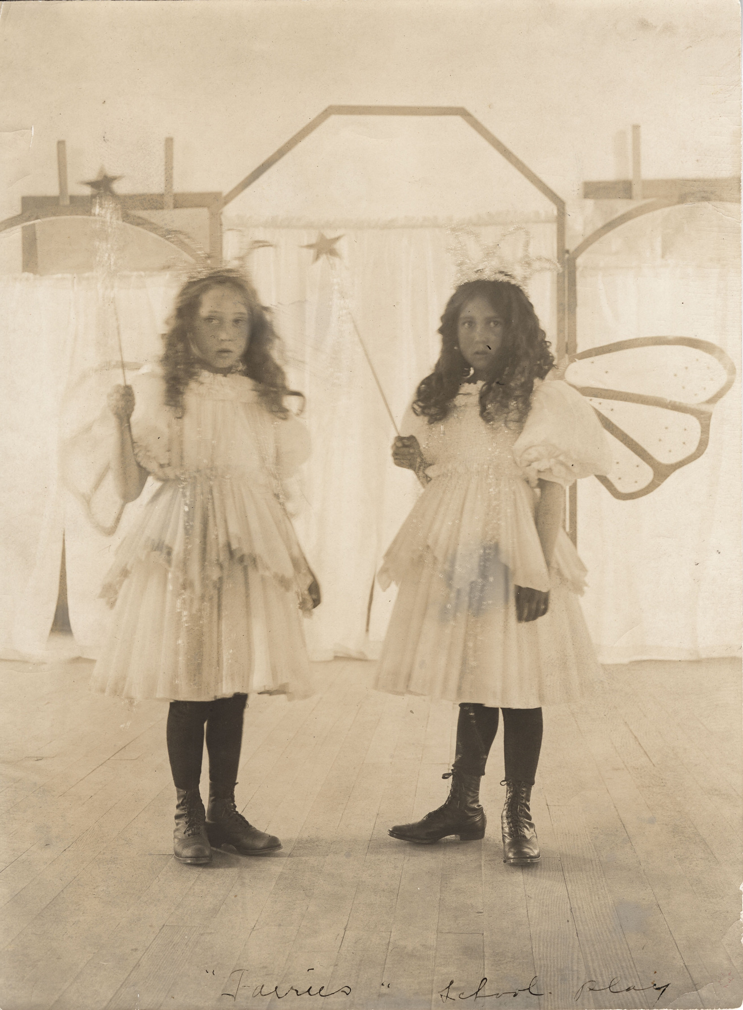 Black and white photograph of two girls in white dresses and wings looking into the camera