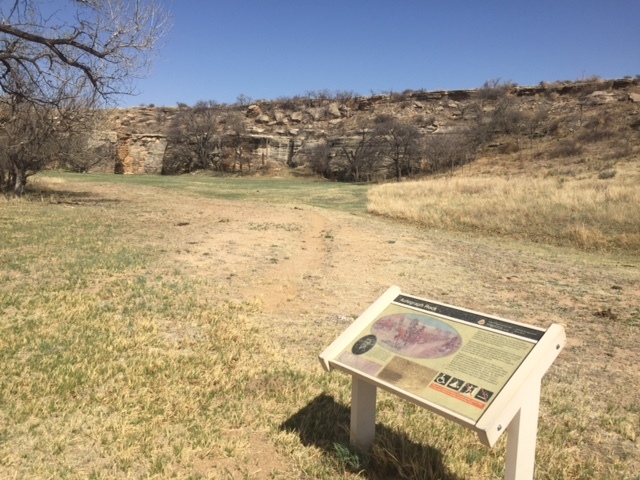 A sign with the text "Autograph Rock" in the right side of a grassy field along a trail.