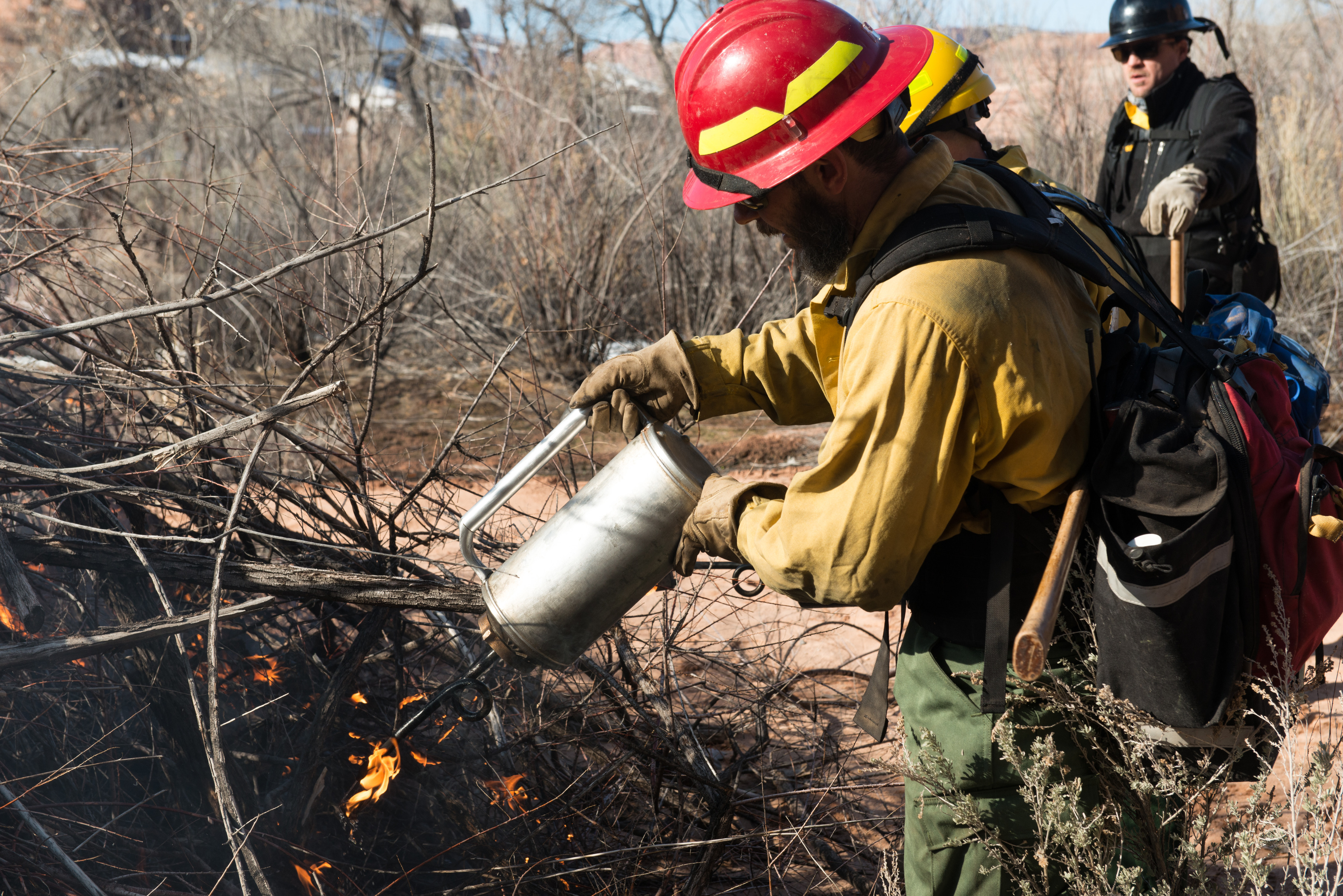 a firefighter holds a drip torch above a pile of dried vegetation
