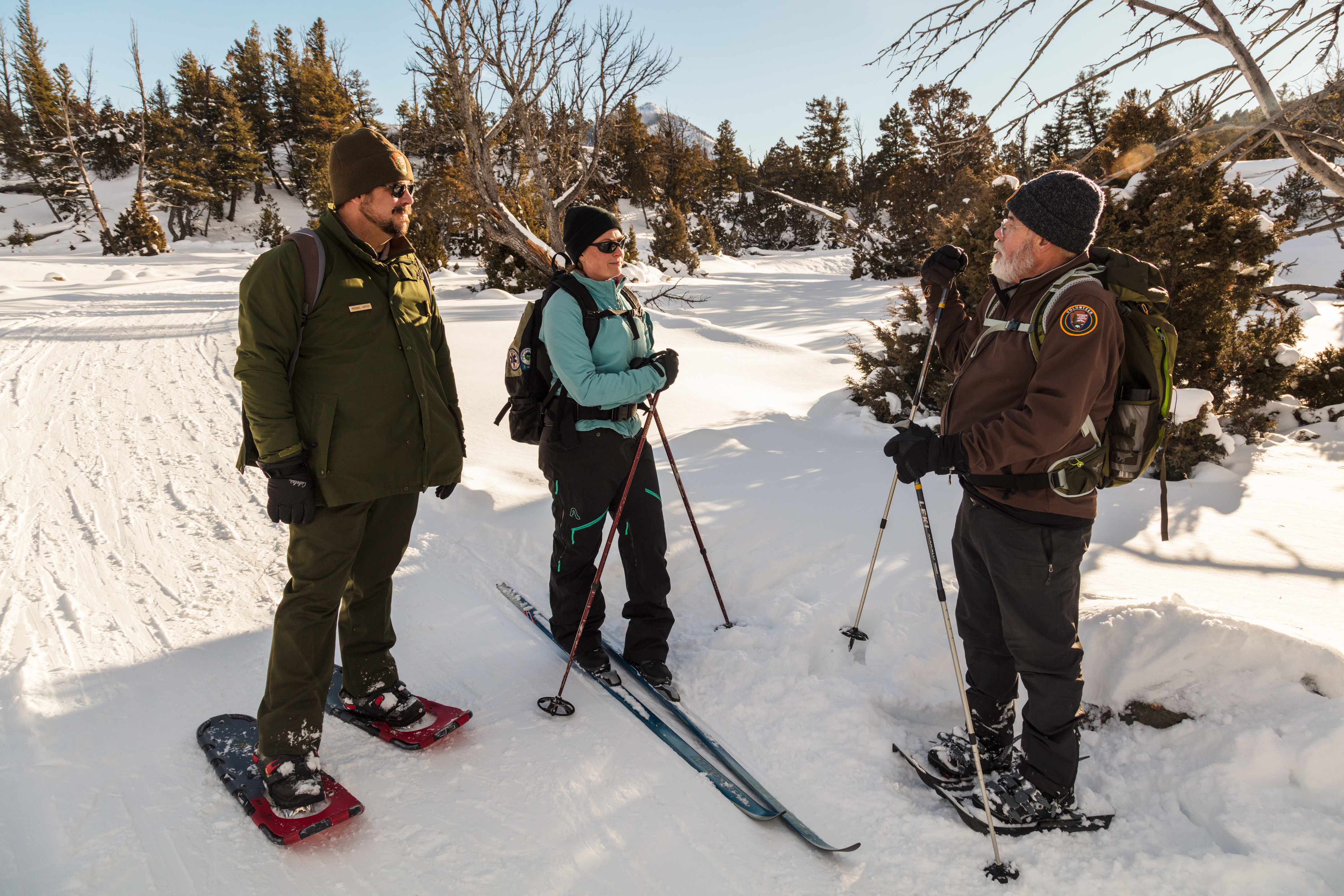 Two men in uniform and on snowshoes talks with a woman on skis
