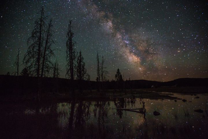 The Milky Way and stars are reflected on the surface of a lake in backcountry at Yellowstone National Park, Wyoming.