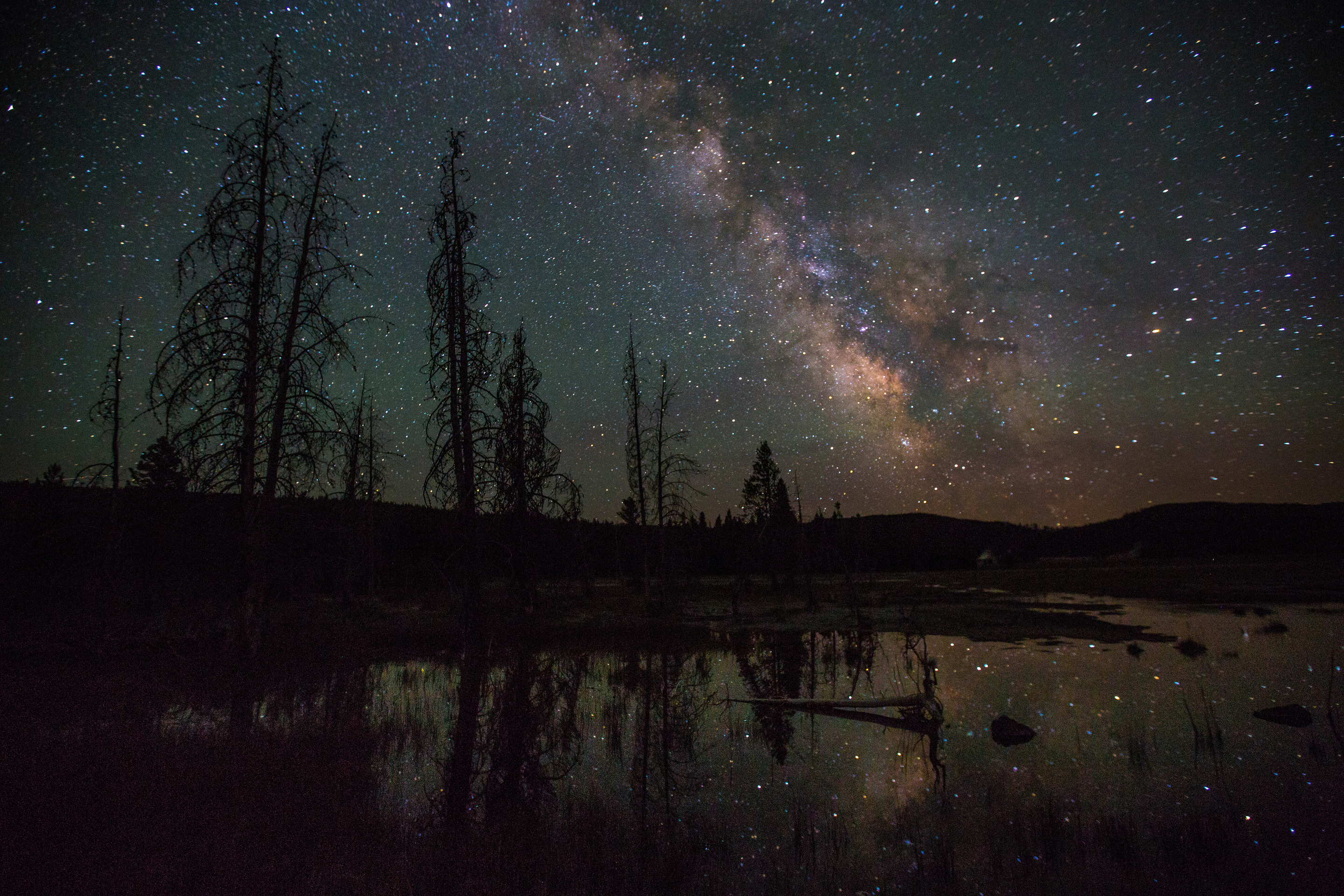The Milky Way and stars are reflected on the surface of a lake in backcountry at Yellowstone National Park, Wyoming.
