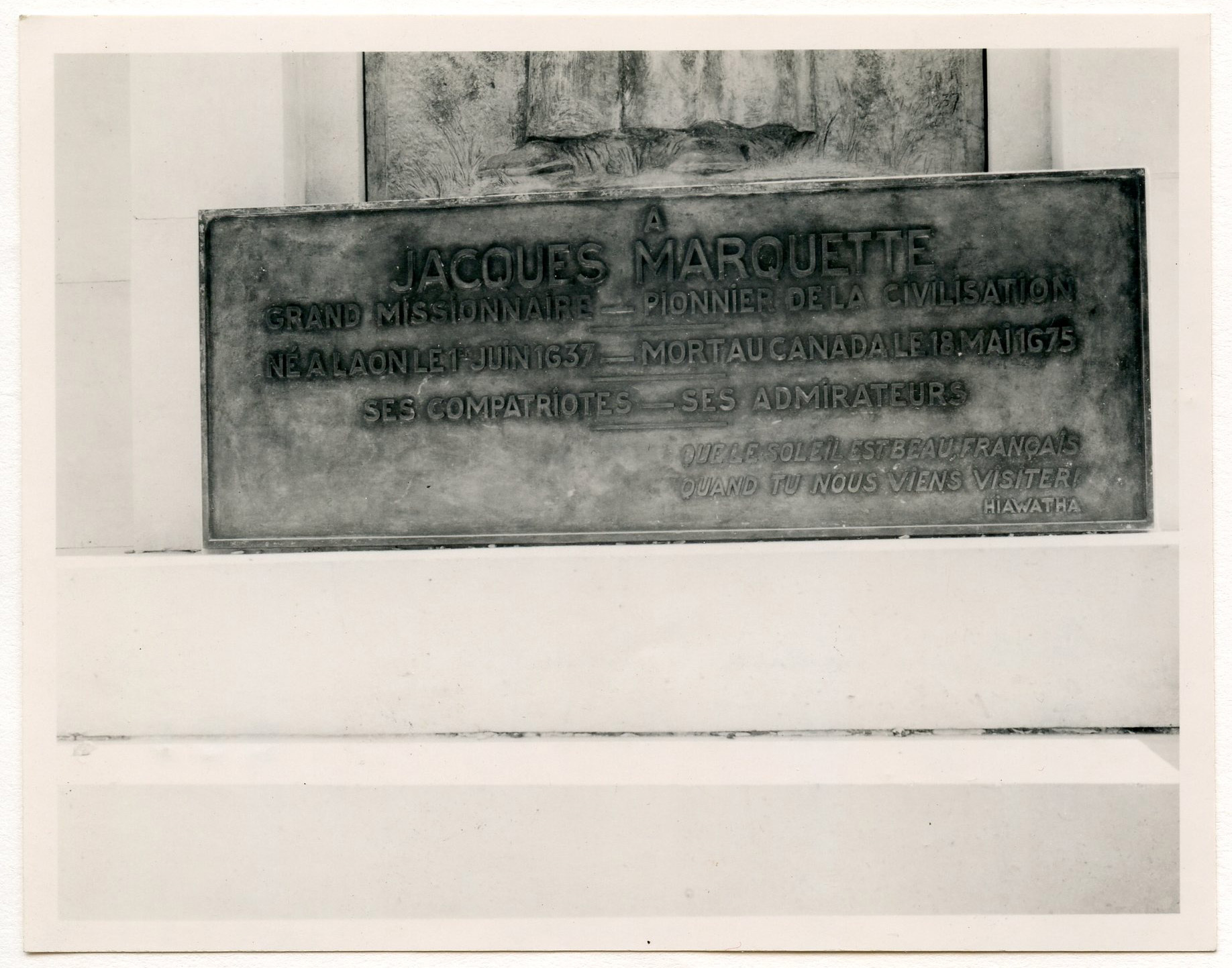Close-up detail of bronze plaque dedicated to a man named "Jacques Marquette." Inscription in French reads: "A Jacques Marquette / Grand missionnaire - Pionnier de la civilisation / Ne a Laon le 1er Juin 1637 - Mort au Canada le 18 Mai 1675 / Ses compatriotes - Ses admirateurs / Que le soleil est beau, Francais / quand tu nous viens visiter! / Hiawatha."