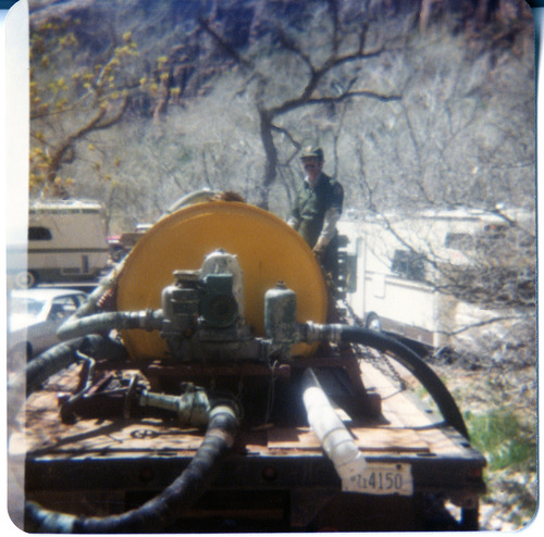 Man standing near sealcoating tank during road work.