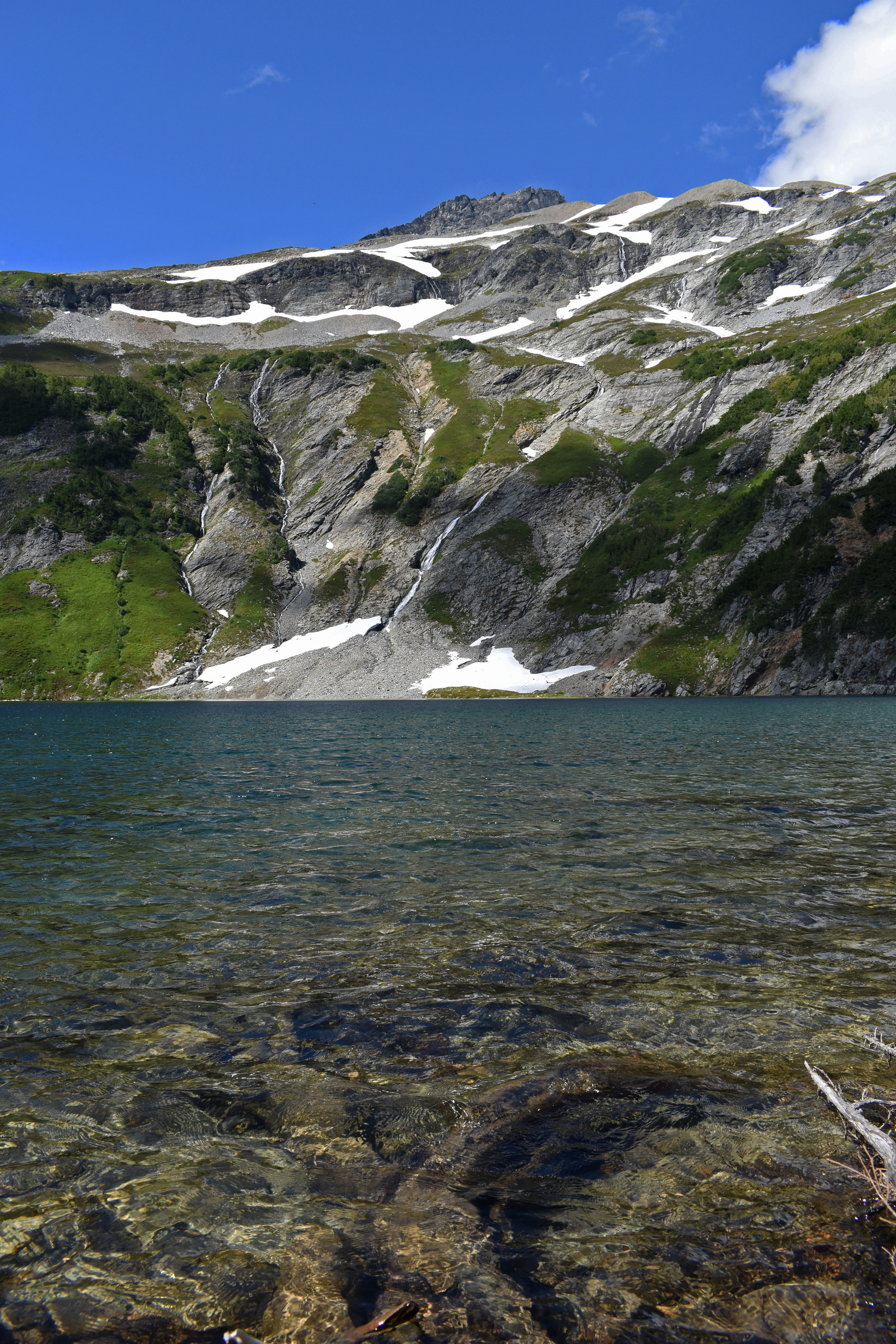 The view of clear blue lake water with some gray cliffs in the background.