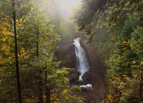 A large waterfall plunges off a sandstone cliff, as viewed from above.