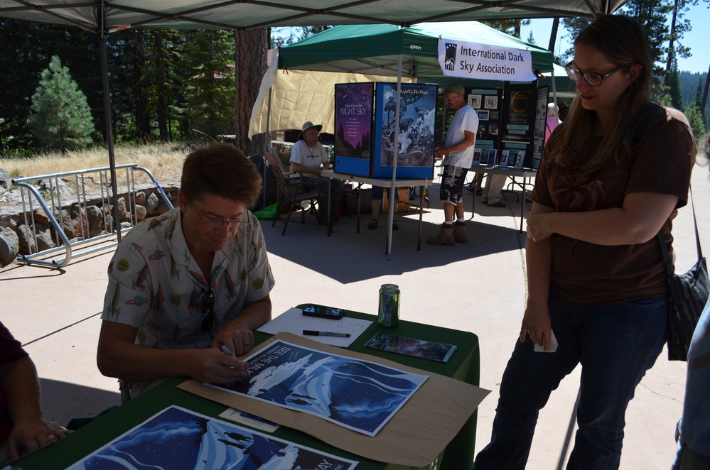 Astronomy lecturer and artist Tyler Nordgren signs illustrated posters he designed of Lassen Volcanic National Park at night.