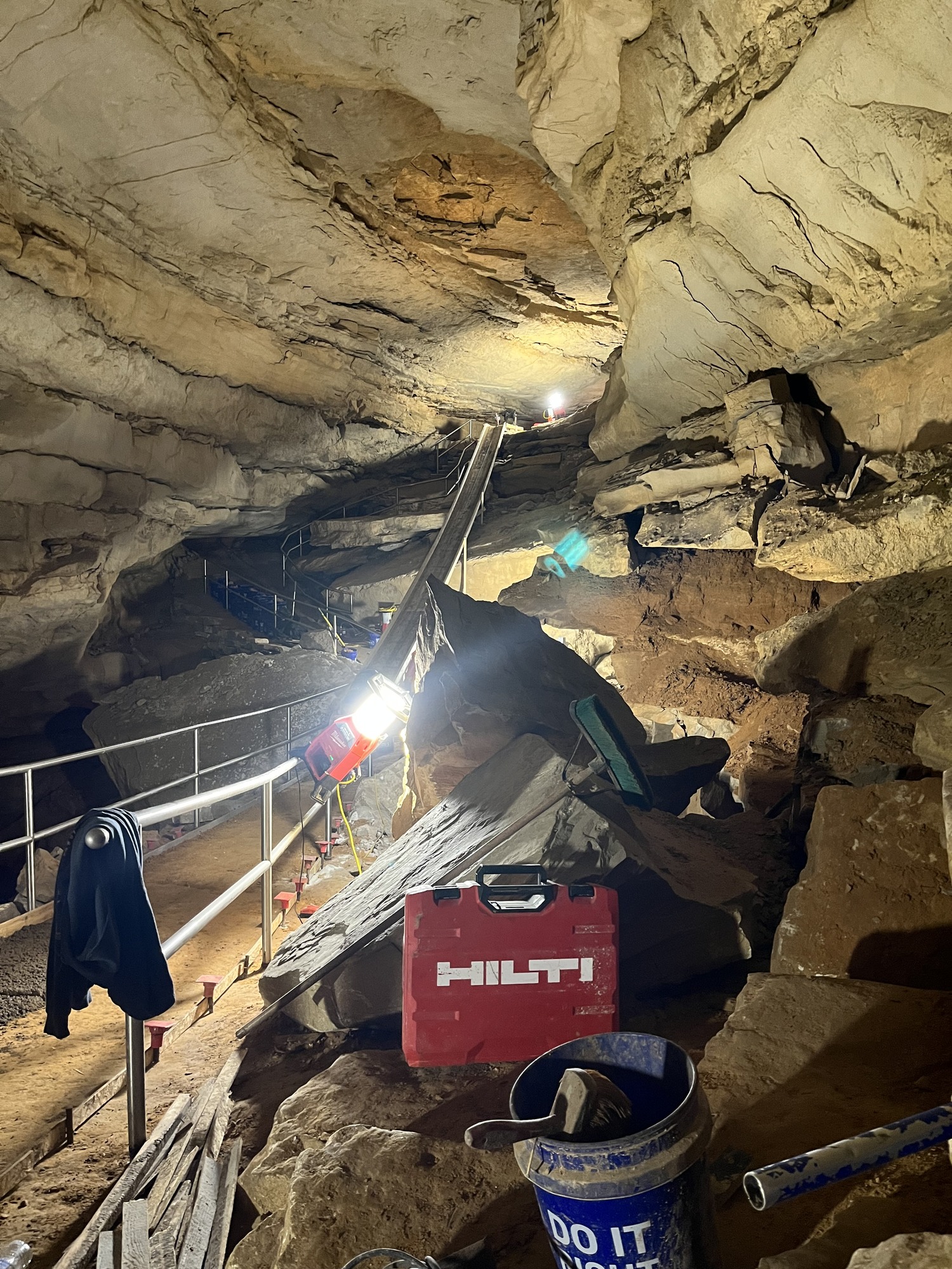 A long slide extends from near the ceiling of a large cave down to a lower walkway.