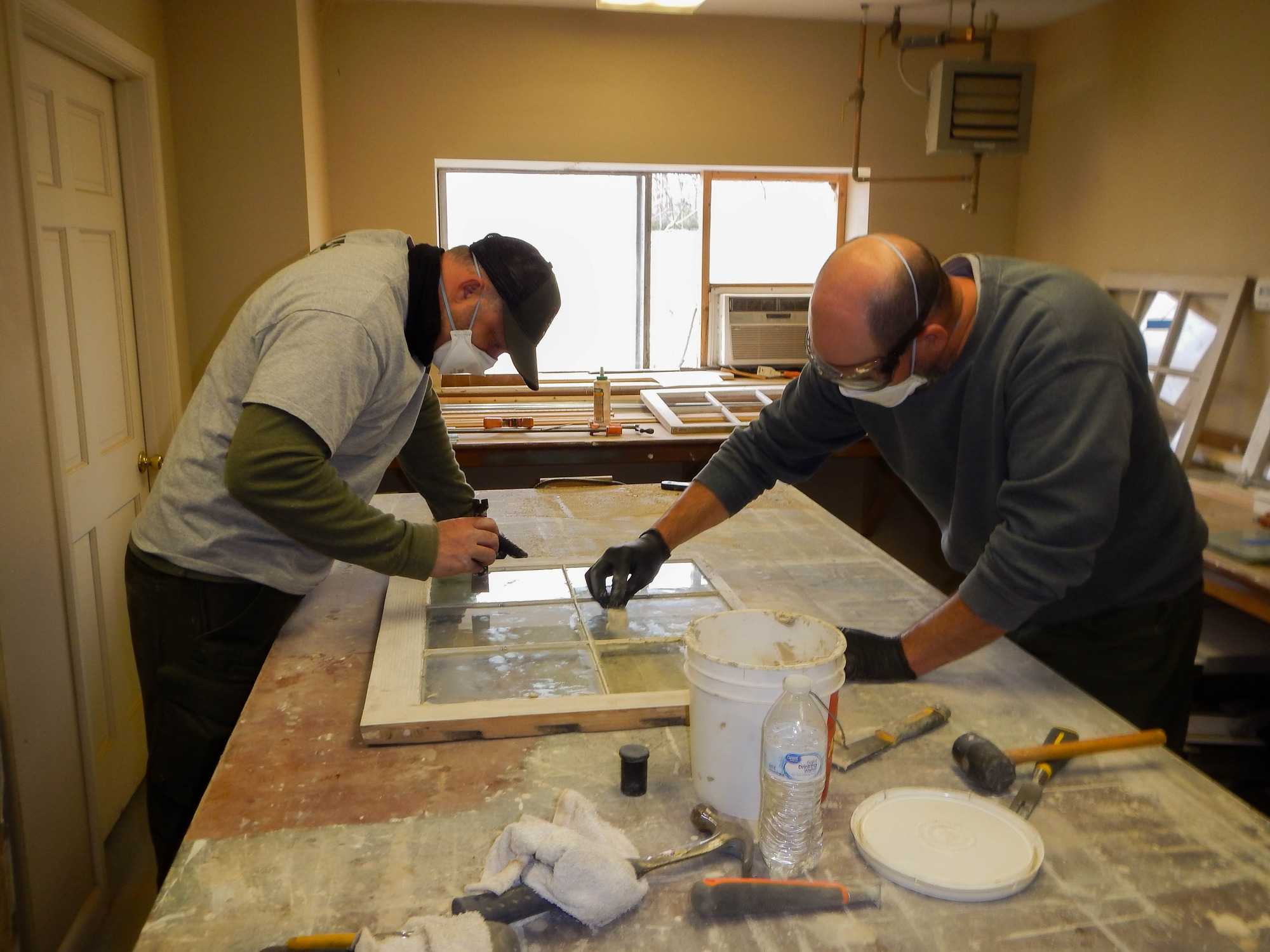 Two men repairing window sashes on a countertop. 