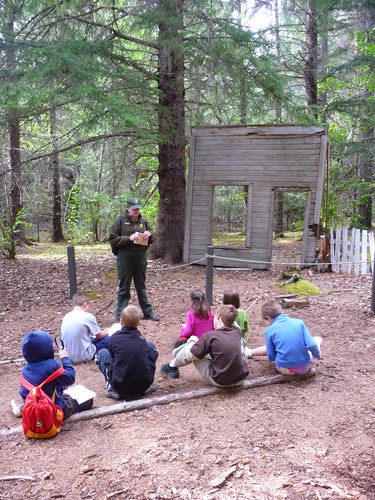 Young students sit while ranger talks to them in a forest setting with historic ruins