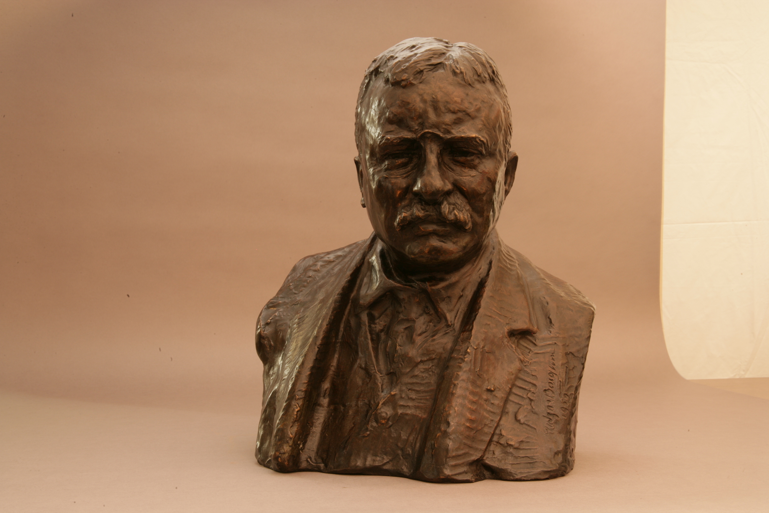 A bronze bust of Theodore Roosevelt. He is wearing pince-nez glasses and a suit. He has a mustache and a serious expression. 