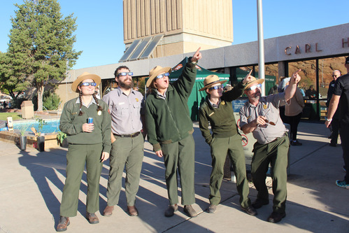 Five park rangers wearing solar glasses point up into the sky.