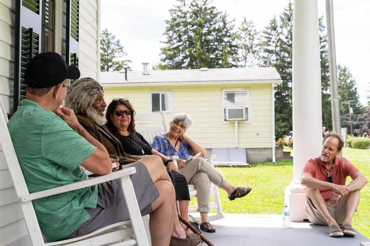 Frederick Douglass sits on a porch with park visitors.