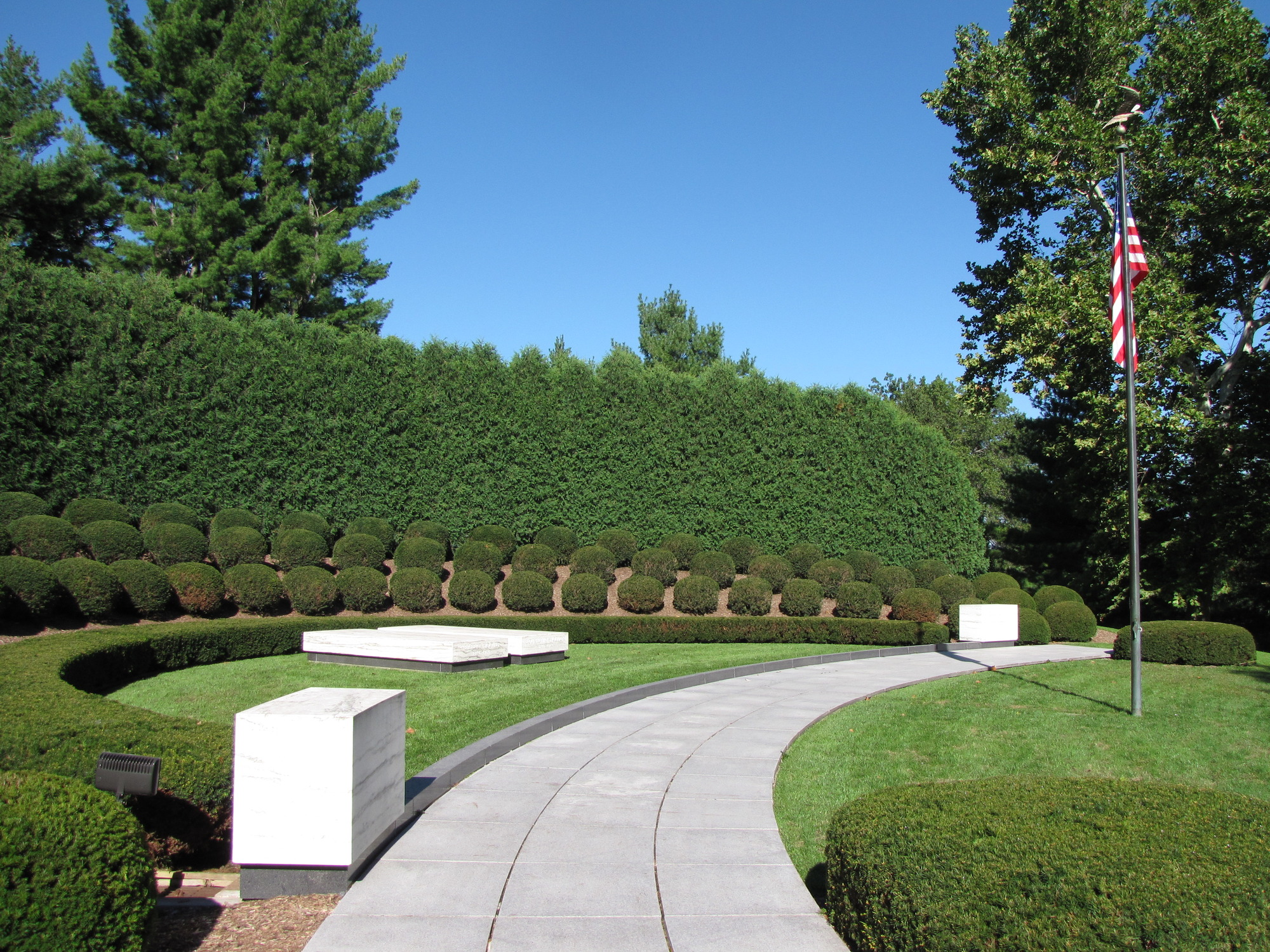 Two plain marble ledgers mark graves in a semicircular planting of shrubs with a US flag.