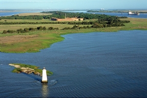 Lighthouse surrounded by water, an island in the background. 