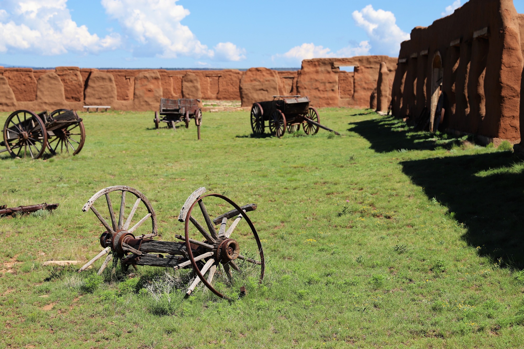 Wagons on green grass surrounded by red adobe walls. 