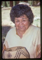 A woman in a Native American attire holds a woven basket.