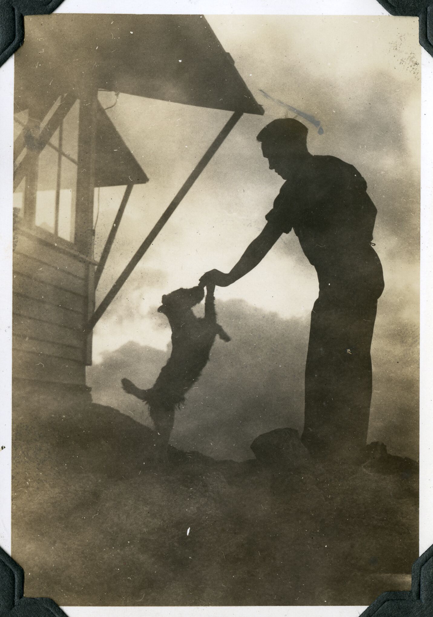 A man  and dog silhouetted against a cloudy sky outside a wooden structure with large windows.