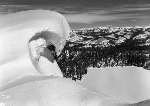 Overhanging Rock snow cornice on Horse Ridge. [From the tip of Horse Ridge, Ostrander Lake looks like a soft white blanket among the lodgepole pine trees. The Ostrander Lake Ski Hut may be seen beyond the Lake, while beyond extends a sea of High Sierra peaks more spectacular in winter than any other time of year].