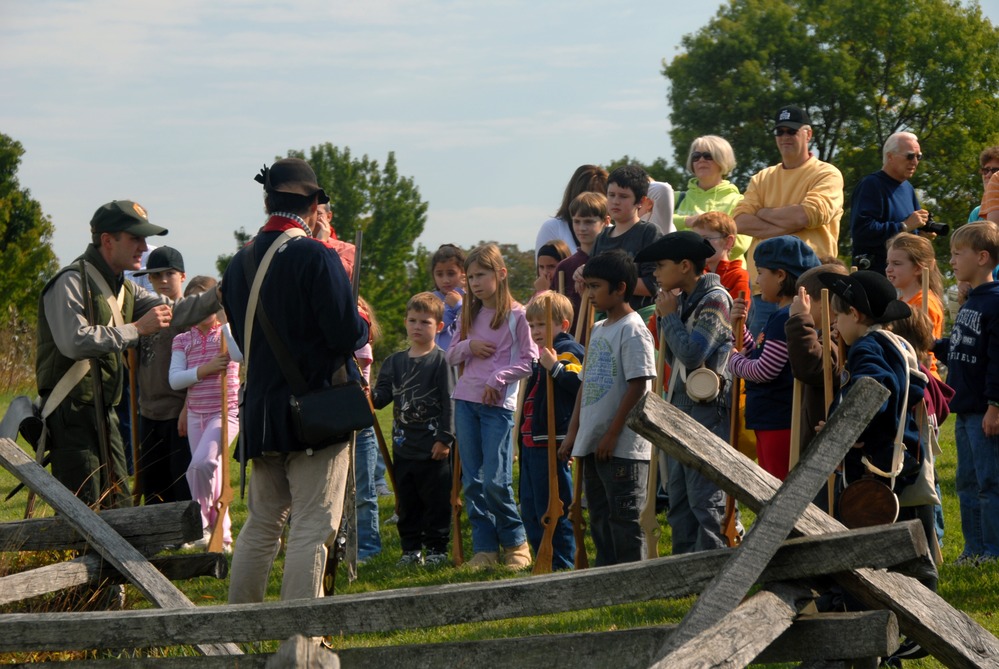 The recruits listen to the soldier at Muhlenberg Brigade cabins