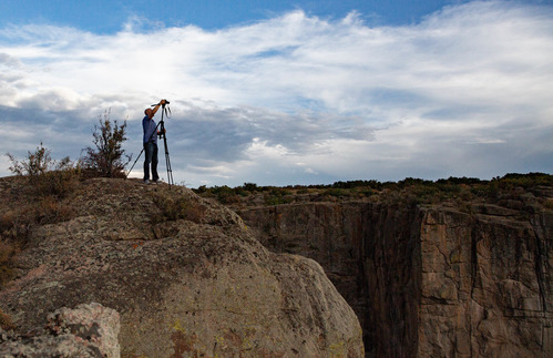 Photographer on a cliff face adjusting his camera on tripod