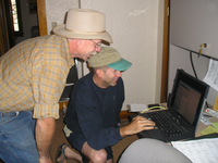 Ron and speaker at 90th celebration viewing computer. Ron Fankhauser and Wilson Burnham