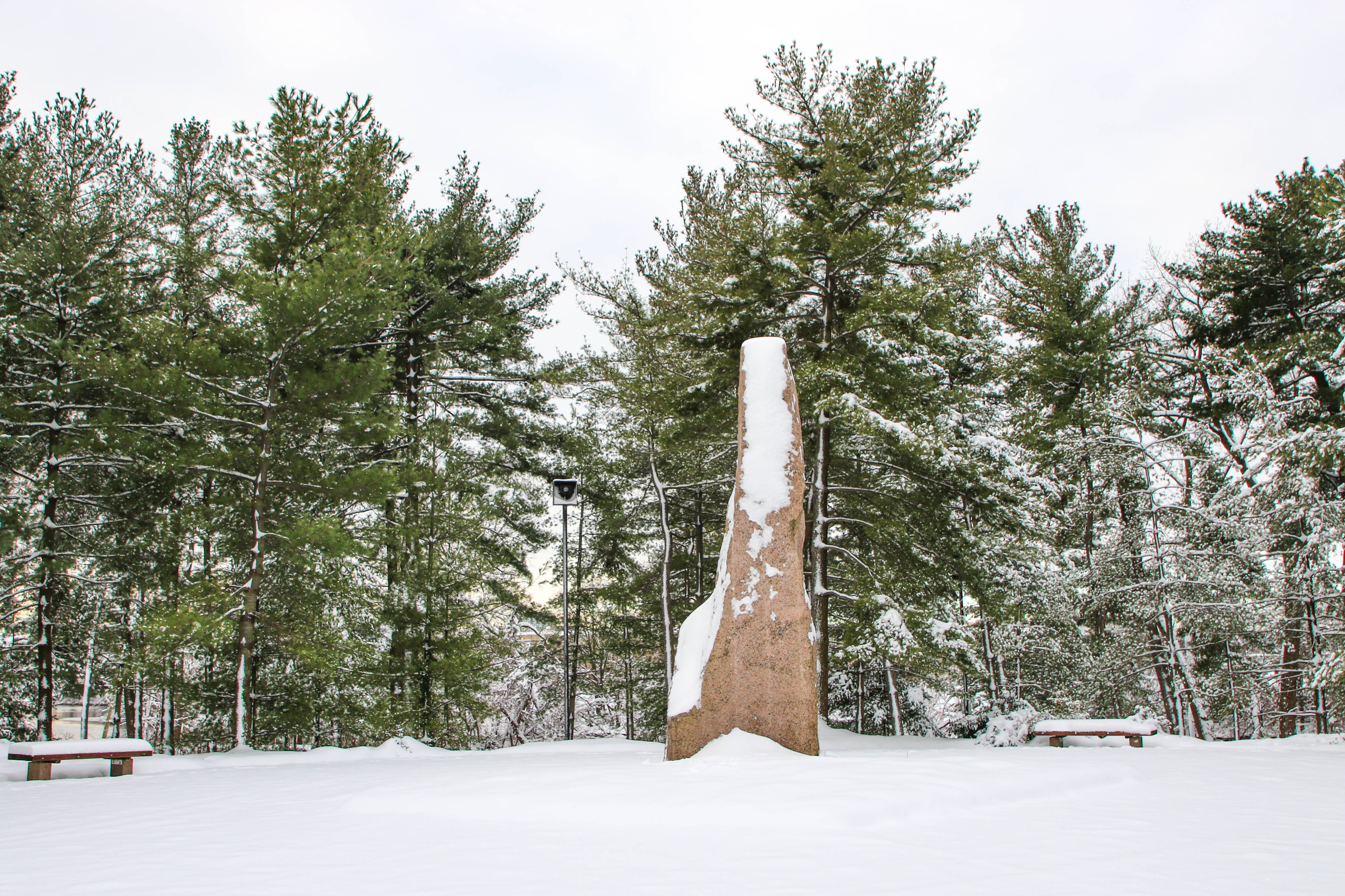 Granite monolith on a plaza surrounded by trees after a snowfall