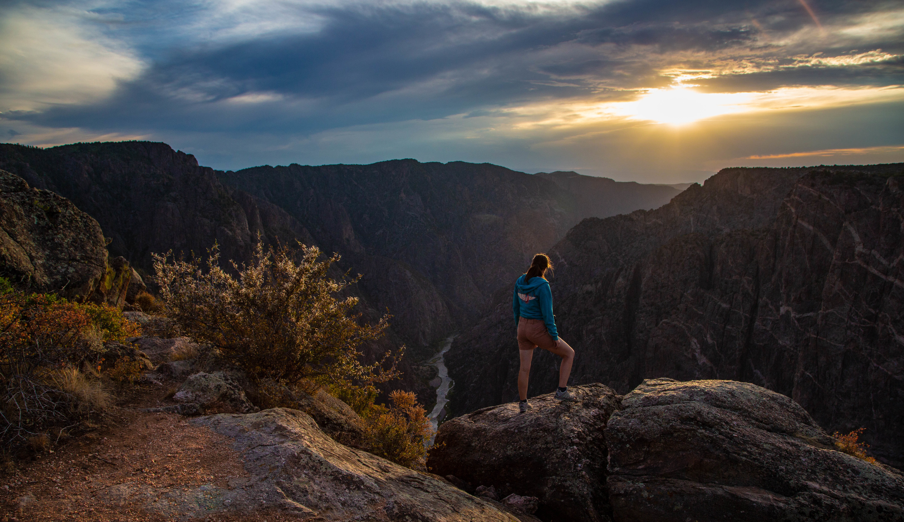 Visitor standing on a rock ledge over a canyon at sunset