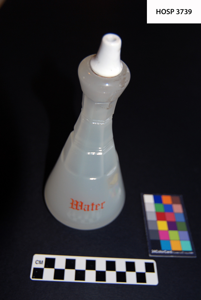 Long neck pressed white glass bottle, white porcelain stopper.  Lettered in red on front "WATER" 