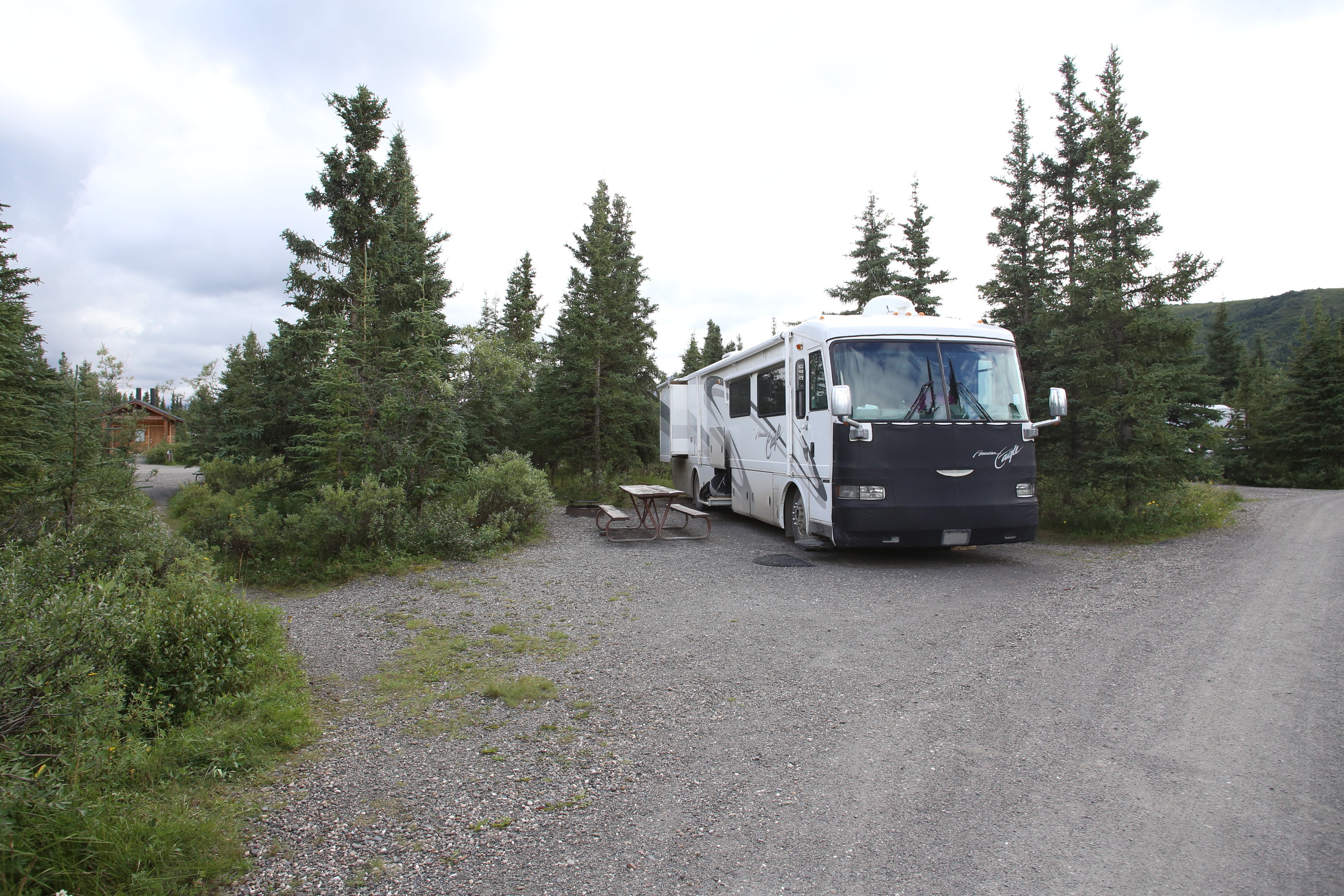 a large R V parked among spruce trees 