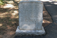 A rough cut granite monument shaped like a tombstone, sits on a rectangular granite base, next to a paved path and a natural area. The monument has an inscription of Griffin Fauntleroy's service in all caps : "THIS SITE WAS OCCUPIED BY THE 1ST VIRGINIA CAVALRY UNDER LIEUTENANT COLONEL WILLIAM WASHINGTON, CONT'L. LINE, AND IT WAS HERE CAPTAIN GRIFFIN FAUNTLEROY, 1ST. VA. LT. DRAGOONS, CONT'L LINE -- WAS MORTALLY WOUNDED ON MARCH 15, 1781. BORN SEPTEMBER 28, 1754. NORTHUMBERLAND CO., VA. 