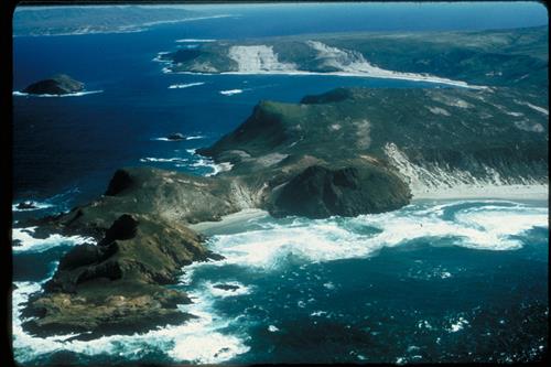 Lester and Harris Points, San Miguel Island with Cuyler Harbor, Prince Island and the western end of Santa Rosa Island in the background. White water in foreground as waves break upon rocky shoreline.