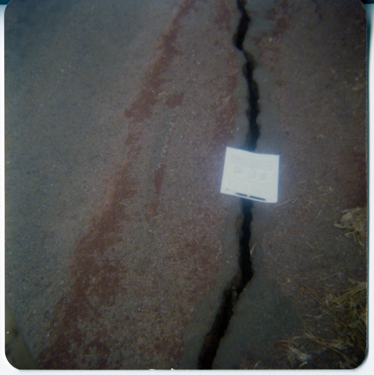 Crack in road in need of repair with paper marking over top.