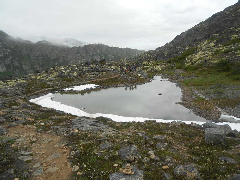 Hikers in the distance next to a pond surrounded by mountains