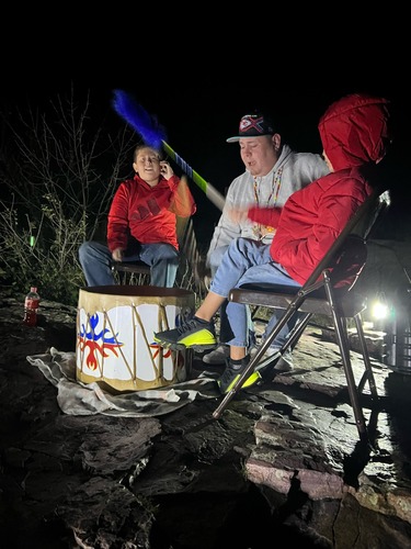 A man beating a drum outside at night between his two small boys.