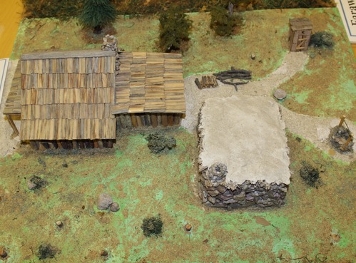 Model log cabin and stone fort, with a well and outhouse. 