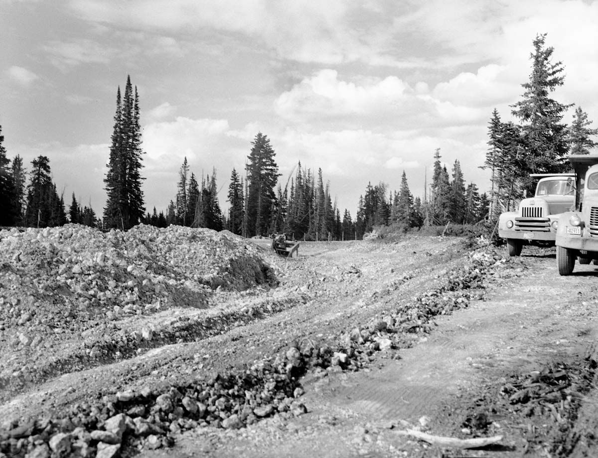 Bulldozer moving rocks at cut at top of Dugway Hill, dump trucks parked waiting to haul rock away.