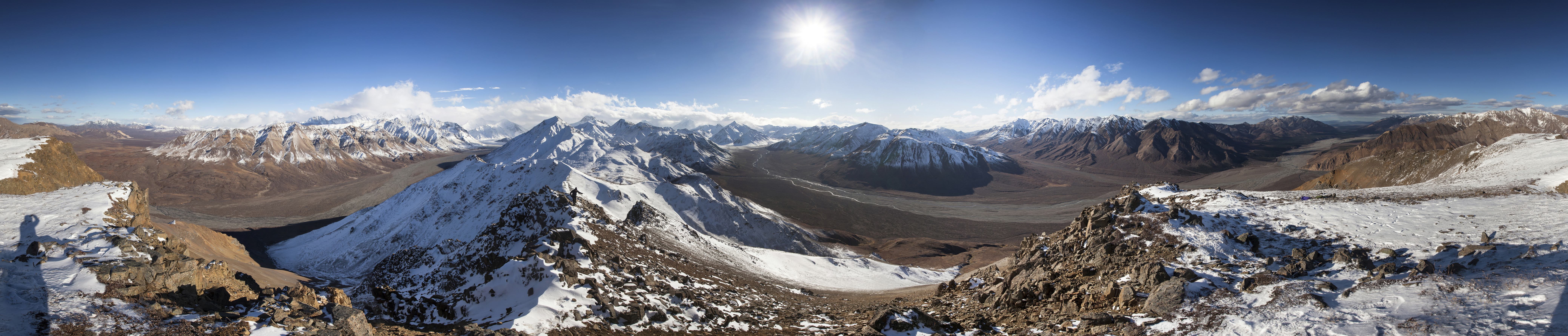 View from atop a snow-dusted mountain, of other snowy mountains and wide river plains