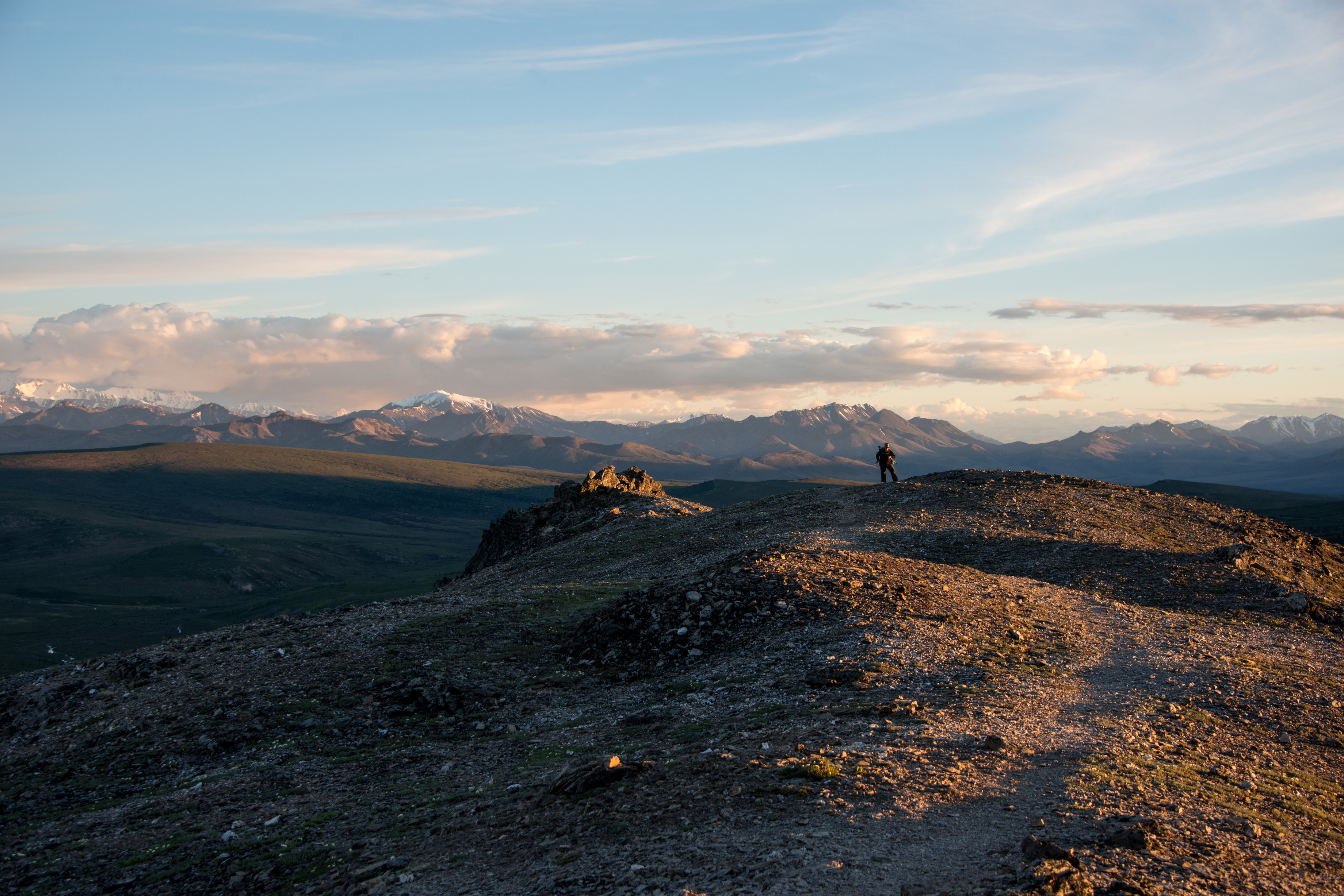 hiker on a mountain top tinged pink by late night sun