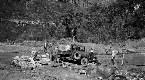 Basket dam #2 construction along the Virgin River with a view of workers unloading boulders from the bed of a pickup truck.