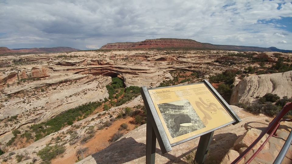 a sign reading Kachina Bridge overlooking a canyon. The bridge is in the distance.