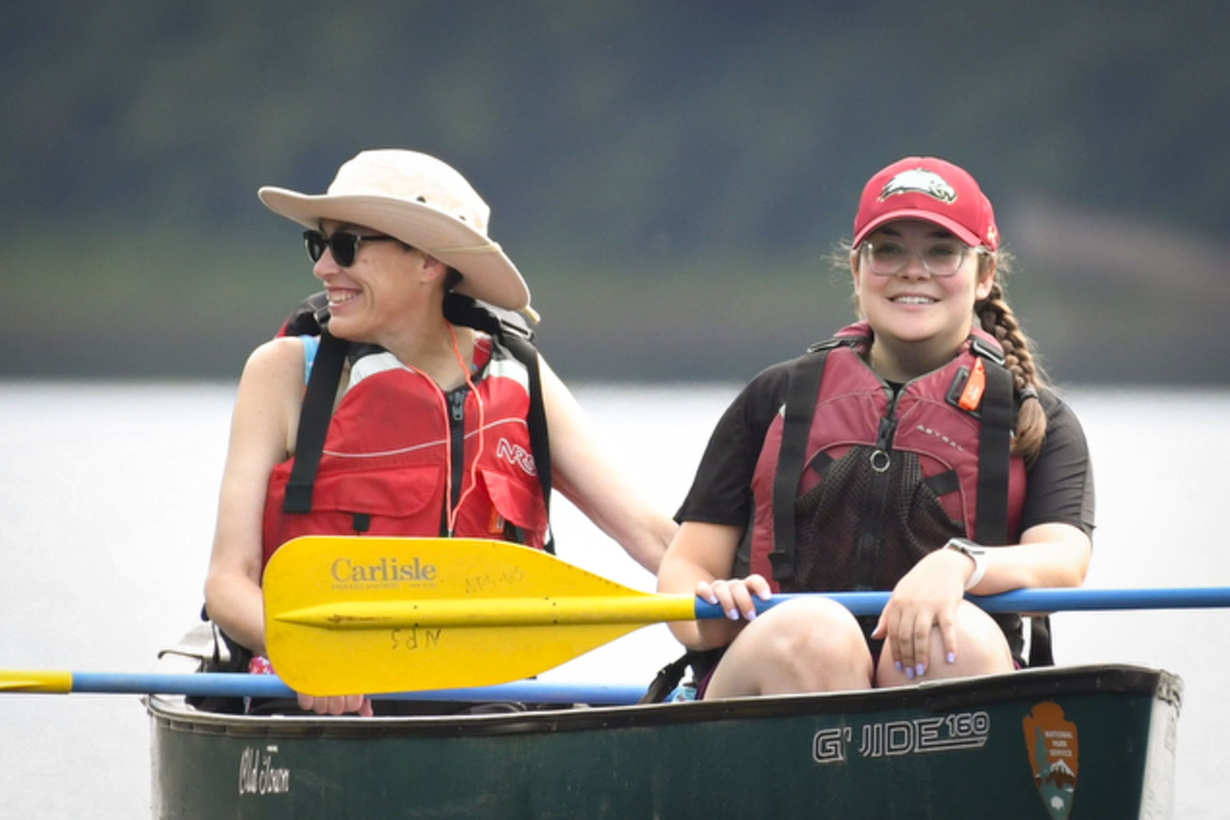 Two people wearing life jackets sit in a canoe with paddles on their laps.