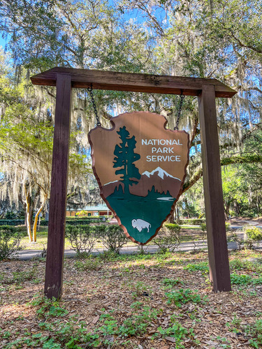 Hanging National Park Service arrowhead sign with a visitor center in the distance 