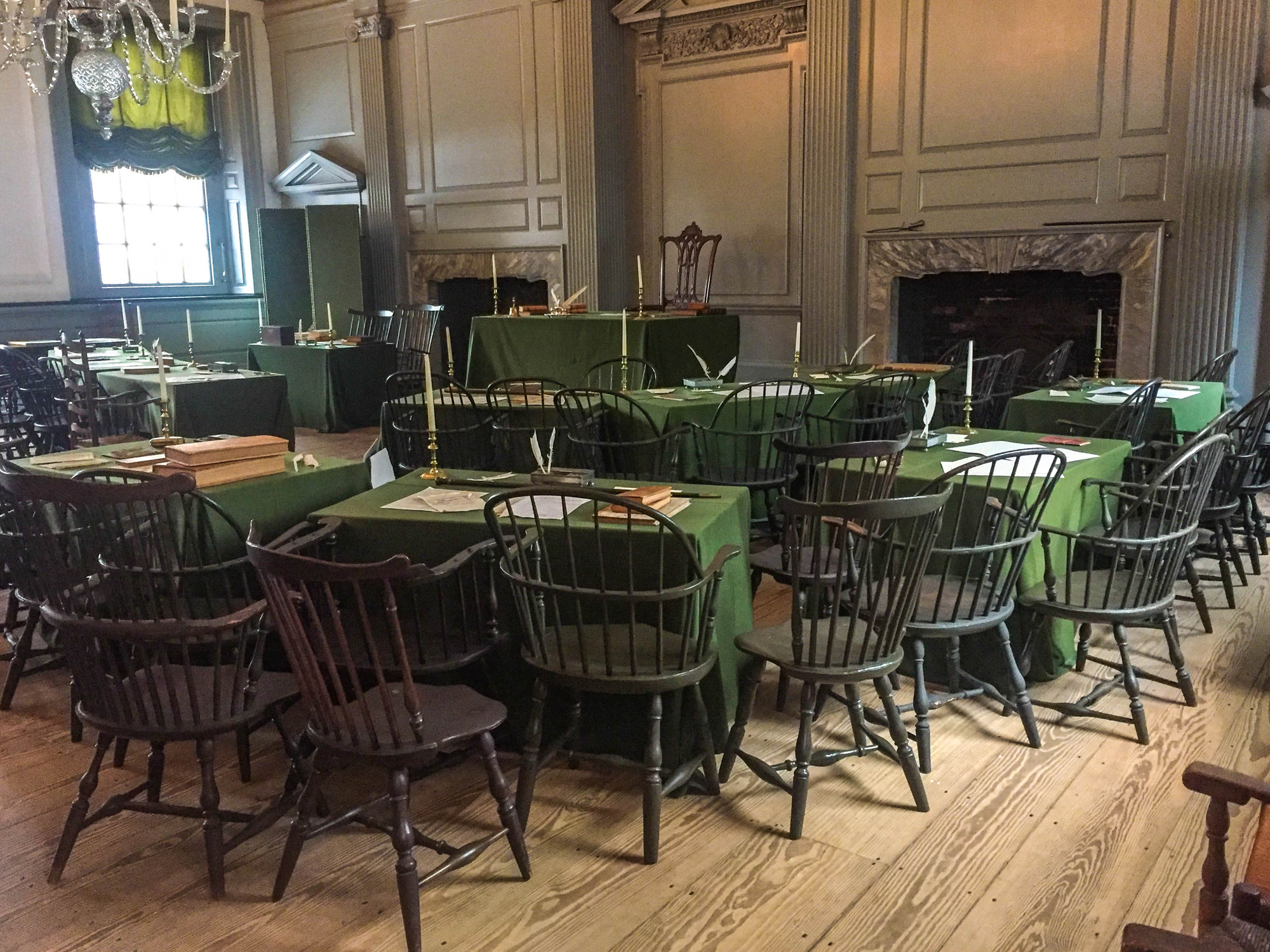 Meeting room with lines of tables and chairs covered with green table cloths, candles, books, papers, and quill pens