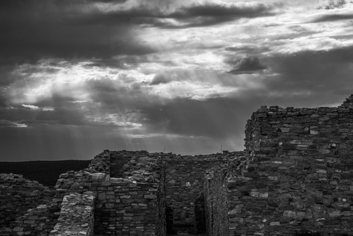 Infrared imge of sunset at Gran Quivira. Mission walls in the foreground with cloudy skies and faint light shining down from the skies.  